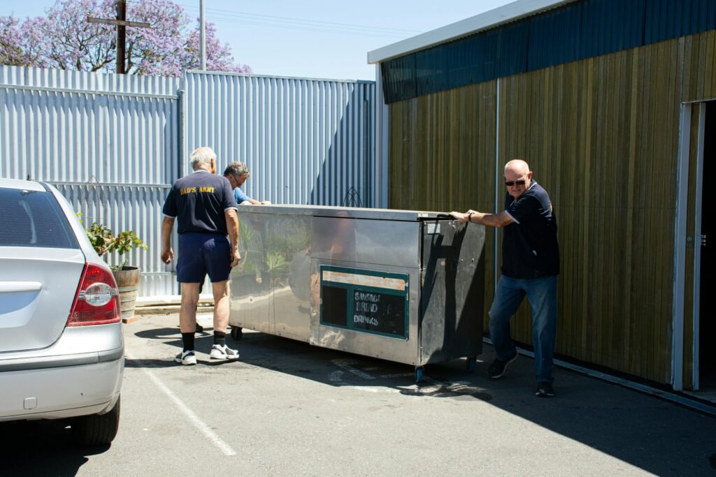 Three men moving large equipment outside a building.